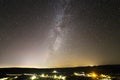 Beautiful starry dark night sky over rural landscape. Dark green hills, bright lights of road. Royalty Free Stock Photo