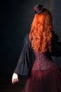 Beautiful steampunk woman back. Slender red-haired girl in corset and hat