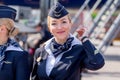 Beautiful stewardess dressed in official dark blue uniform of Aeroflot Airlines on airfield. Passenger jet aircraft on background.
