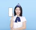 Beautiful stewardess showing the mobile phone with blank screen on blue background Royalty Free Stock Photo