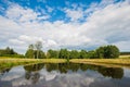 Beautiful still lake with trees on the horizon and white puffy clouds in the sky. Peaceful summer day at the cottage. Large green Royalty Free Stock Photo