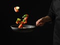 Beautiful still life of red fish with vegetables, cut into pieces and a black background. The cook holds a frying pan with red Royalty Free Stock Photo