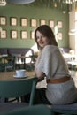 Beautiful stilysh woman sit in cafe and smiling. Girl at round table in cafe. Vertical frame