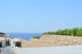 Stone wall descending down to the sea with blue water in a tropical resort and a white building with a roof of red shingles and gr