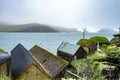 Beautiful stone and wooden houses green grass on the roof, sea side next to blue ocean and Drangarnir in the background foggy Royalty Free Stock Photo