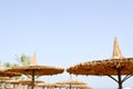 Beautiful straw sun umbrellas in the form of hats and green palm trees in a tropical desert resort against the blue salt sea Royalty Free Stock Photo