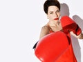 Beautiful and strong brunette woman with short hair in red dress, earrings and boxing gloves punches hits Royalty Free Stock Photo