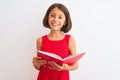 Beautiful student child girl reading red book standing over isolated white background with a happy face standing and smiling with Royalty Free Stock Photo