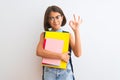 Beautiful student child girl wearing backpack glasses books over isolated white background doing ok sign with fingers, excellent Royalty Free Stock Photo