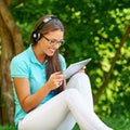 Beautiful student girl with gadget listening to the music in summer park