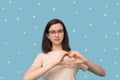 Beautiful student girl in glasses makes a heart shape with her hands, smiles on blue background. Love, relationships Royalty Free Stock Photo