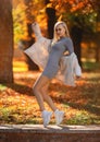 Beautiful student girl with perfect legs sitting on the parapet in the autumn park in white sneakers and coat Royalty Free Stock Photo