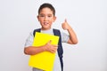 Beautiful student kid boy wearing backpack holding book over isolated white background pointing and showing with thumb up to the Royalty Free Stock Photo