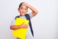 Beautiful student kid boy wearing backpack holding book over isolated white background stressed with hand on head, shocked with Royalty Free Stock Photo