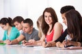 Beautiful student sitting with classmates writing at desk Royalty Free Stock Photo