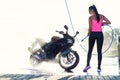 Beautiful stunning girl washes a motorcycle in self service carwash with high pressure water jet in morning at sunrise.