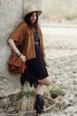 beautiful stylish boho woman with hat, leather bag, fringe poncho and boots. girl in gypsy hippie look young traveler posing near Royalty Free Stock Photo