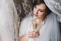 Beautiful stylish brunette bride posing in silk robe under veil with champagne glass in the morning. Happy woman model with Royalty Free Stock Photo