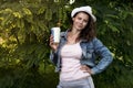 Beautiful stylish fashionable young girl in park with cocktail and straw in her hand. nice woman in hat and jeans jacket in nature Royalty Free Stock Photo