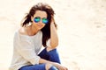 Beautiful stylish female in sunglasses sitting on a beach