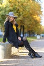 Beautiful stylish girl in autumn park on bench. fashion young woman in hat and coat in fall, outdoors Royalty Free Stock Photo