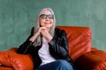 Beautiful stylish senior woman with long straight gray hair, wearing eyeglasses and black leather jacket, sitting in