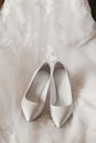 beautiful stylish shoes on luxury silk wedding dress. simple white shoes on white gown with lace floral ornaments, bridal morning Royalty Free Stock Photo