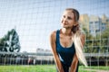 Beautiful stylish woman in a blue shirt and leggings stands near a football goal at the stadium at sunset. Beautiful sunlight. A g