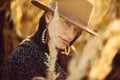 Beautiful stylish woman in brown hat and vintage coat posing in autumn maize field in sunset light. Portrait of fashionable young Royalty Free Stock Photo