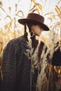 Beautiful stylish woman in brown hat and vintage coat posing in autumn maize field in sunset light. Portrait of fashionable young Royalty Free Stock Photo