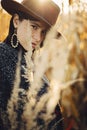 Beautiful stylish woman in brown hat and vintage coat posing in autumn maize field in sunset light. Portrait of fashionable young Royalty Free Stock Photo