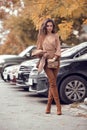 Beautiful stylish woman. Fashion outfit, autumn trend. Young casual brunette walking by cars in street. Fashion girl holding