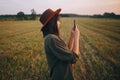 Beautiful stylish woman in hat taking photo of sunset on phone in summer field. Atmospheric moment Royalty Free Stock Photo