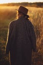 Beautiful stylish woman in hat and vintage coat walking in autumn field in warm sunset light. Tranquil atmospheric moment. Royalty Free Stock Photo