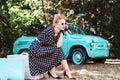 Woman in vintage clothes is sitting on suitcase on background old car. Royalty Free Stock Photo