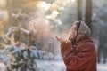 Beautiful, stylish and young girl, blowing the snow from her hands in winter forest. Christmas holiday Royalty Free Stock Photo