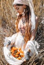 Beautiful stylish young girl holding tangerines in the hem of her skirt on the field