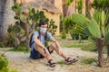 beautiful stylish young man in desert among the cacti, wearing a medical mask during COVID-19 coronavirus, traveling in