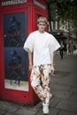 Beautiful and stylish young man in white T-shirt and colored brown training pants in front of red telephone booth. posing during t