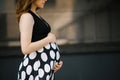 A beautiful stylish young pregnant woman in a black dress with white polka dots holds her hands on her stomach. Happy waiting for Royalty Free Stock Photo