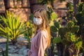 beautiful stylish young woman in pink dress in desert among the cacti, wearing a medical mask during COVID-19 Royalty Free Stock Photo