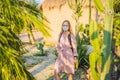 beautiful stylish young woman in pink dress in desert among the cacti, wearing a medical mask during COVID-19 Royalty Free Stock Photo