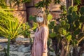 beautiful stylish young woman in pink dress in desert among the cacti, wearing a medical mask during COVID-19 Royalty Free Stock Photo