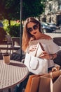 Beautiful stylish young woman with shopping bags chilling in outdoor cafe on city street and checking her purchases. Royalty Free Stock Photo