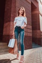 Beautiful stylish young woman with shopping bags walking on city street. Slim model wearing closing and accessories. Royalty Free Stock Photo