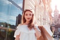 Beautiful stylish young woman with shopping bags walking on city street in summer. Happy girl holding purchases Royalty Free Stock Photo