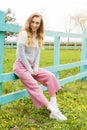 Beautiful stylish young woman sitting on a blue fence on green grass - fashion and style concept Royalty Free Stock Photo