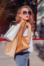 Beautiful stylish young woman walking with shopping bags on city street along showcases and stores. Black friday Royalty Free Stock Photo