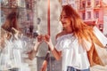 Beautiful stylish young woman walking with shopping bags on city street and looking at showcase of a store Royalty Free Stock Photo