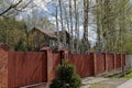 A beautiful suburban two-story wooden house surrounded by white birches behind a long fence